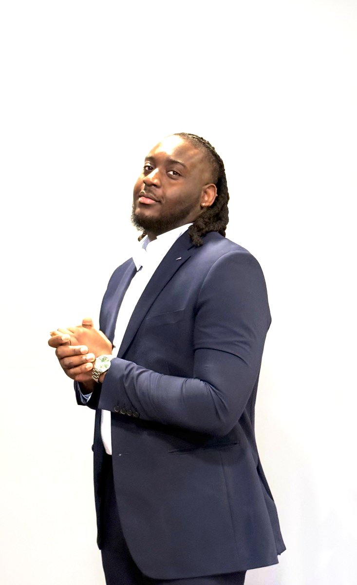 Michael Quarcoopome standing in a navy suit with his hands clasped, looking toward the camera.
