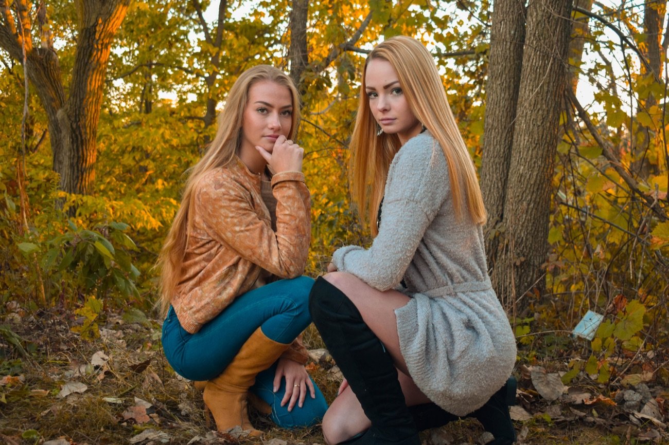 Two women in an autumn woodland, colour graded with warm orange foliage and deep teal tones.