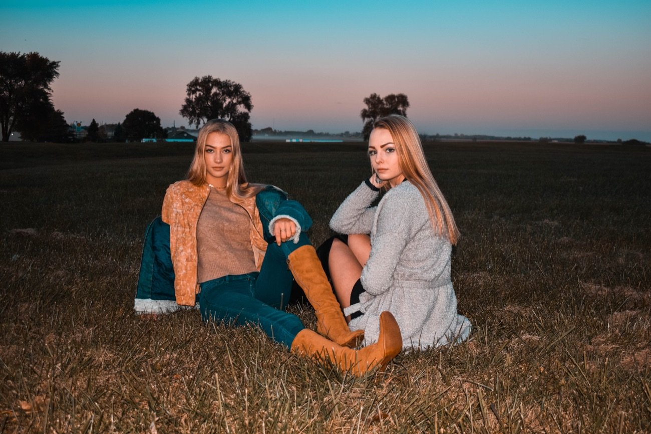Two women seated in a field at dusk, graded with a teal and orange sunset sky.